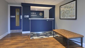 A reception area with a blue wall, a clock, a framed map, and a bench. - Travelodge Stonehouse (Stonehouse)