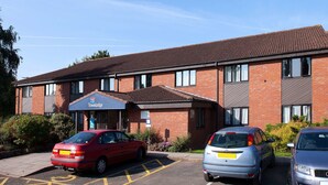 A Travelodge hotel with a brick facade, a parking lot with three cars, and a clear blue sky. - Travelodge Ludlow Woofferton (Ludlow)
