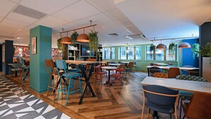 A modern cafe with wooden flooring, colorful chairs, and hanging plants. - Travelodge Edinburgh Central (Edinburgh)