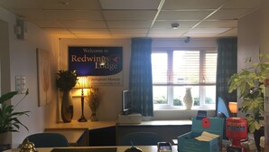 Mostrador de recepción en Redwings Lodge con un cartel, computadora y varios objetos como un teléfono y una caja de donaciones para el poppy appeal.