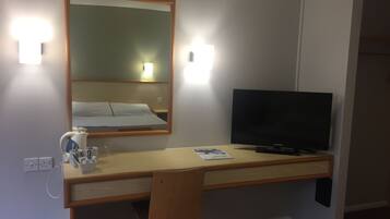 Habitación de hotel con un escritorio de madera, televisor, espejo y cama con ropa blanca.