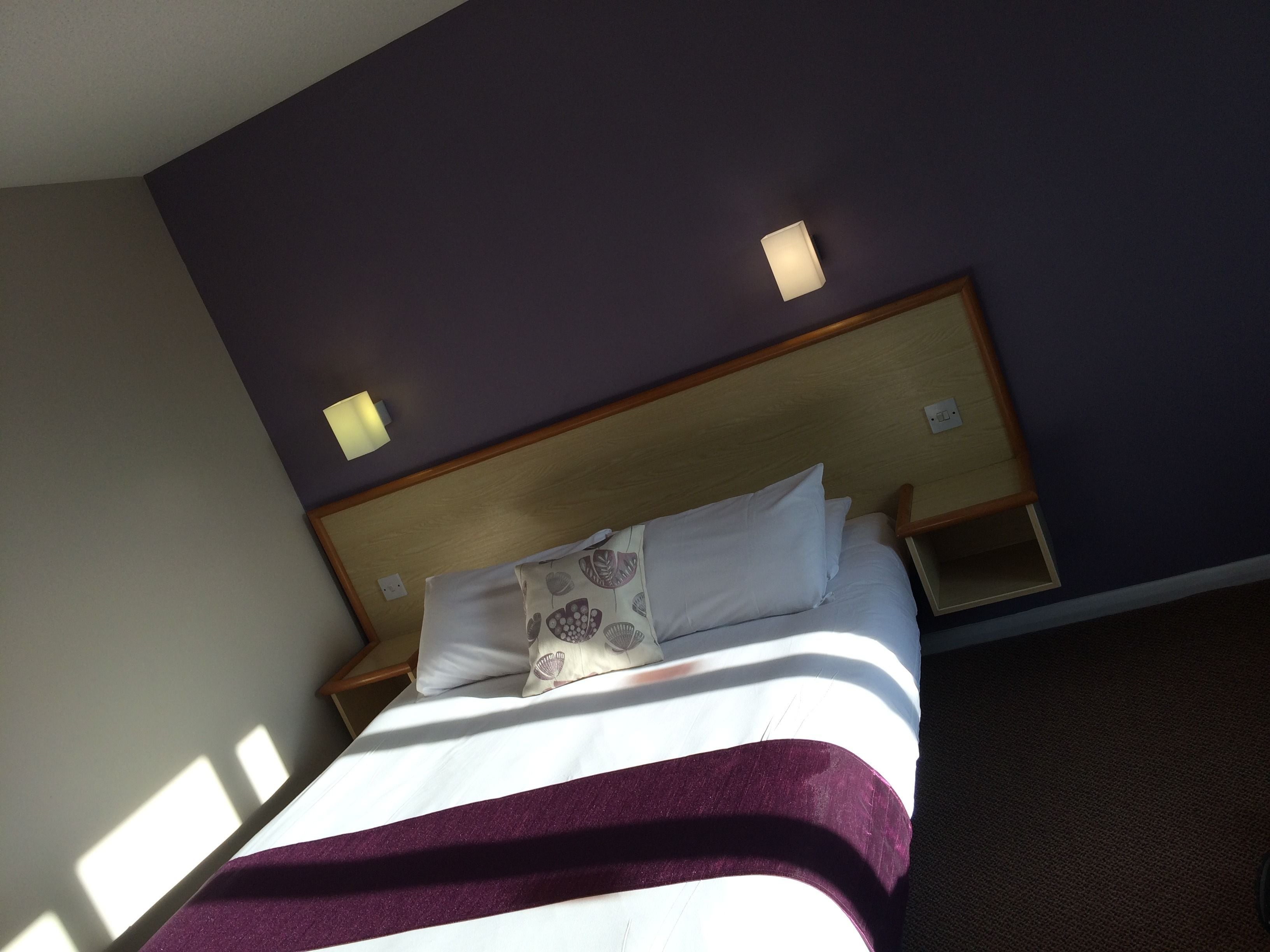 A hotel room with a bed, a nightstand, and a wall-mounted light fixture.