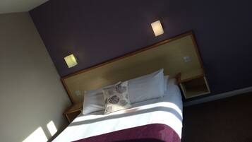 A hotel room with a bed, a nightstand, and a wall-mounted light fixture.