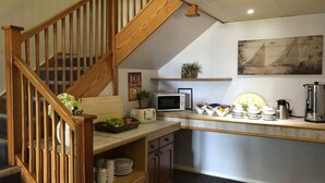Cocina con escalera de madera, armarios blancos, microondas, cafetera y un cuadro en la pared.