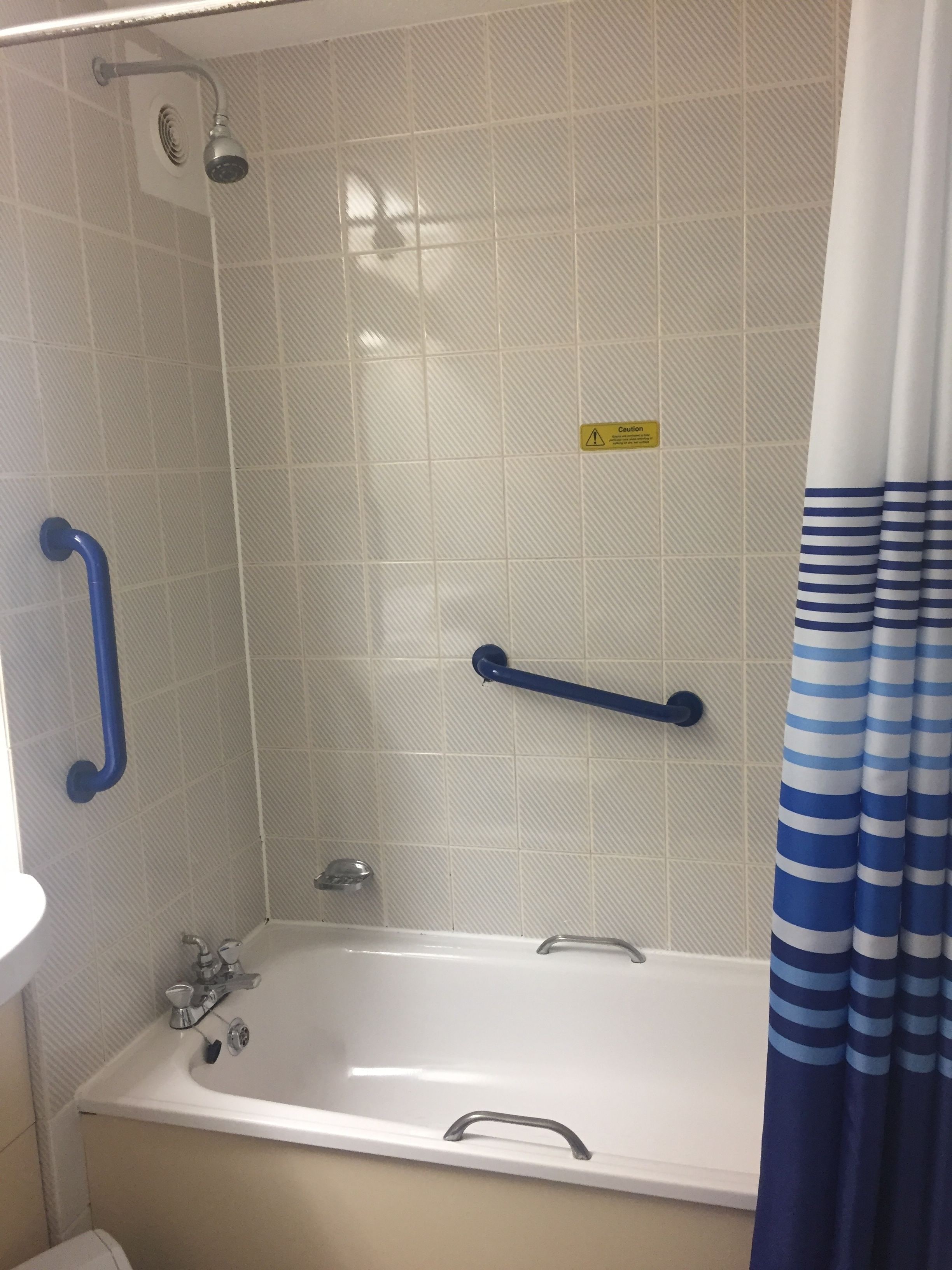 A bathroom with a bathtub, a shower, and a handrail.