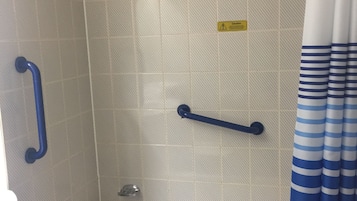 A bathroom with a bathtub, a shower, and a handrail.