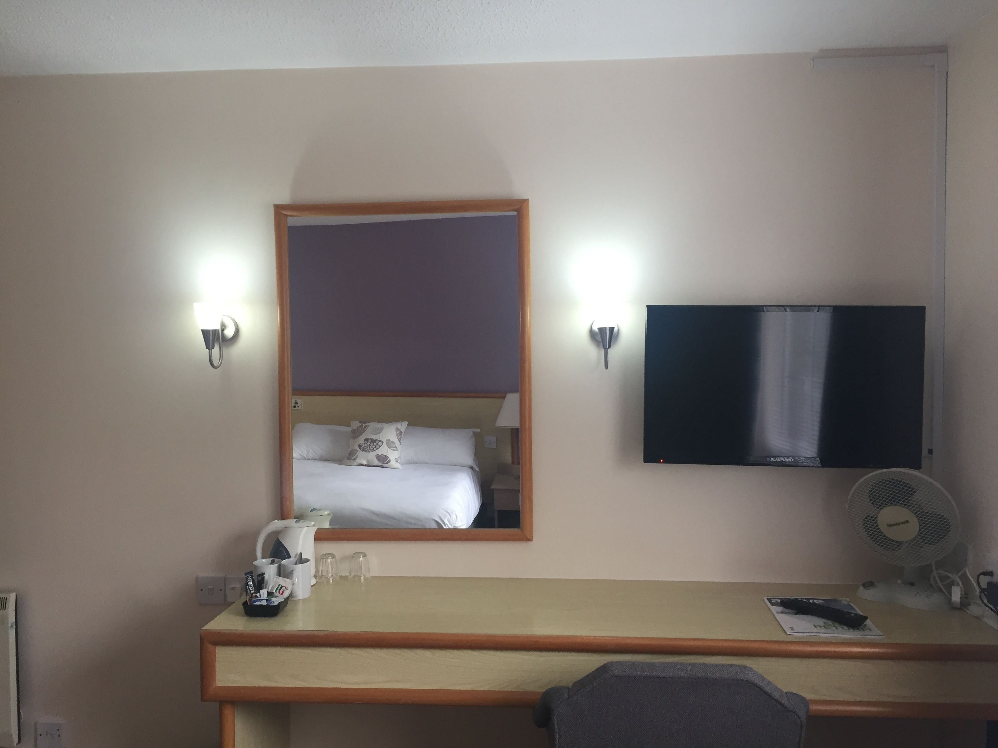 Une chambre d’hôtel équipée d’un lit, d’un bureau, d’une télévision et d’un miroir fixé au mur.