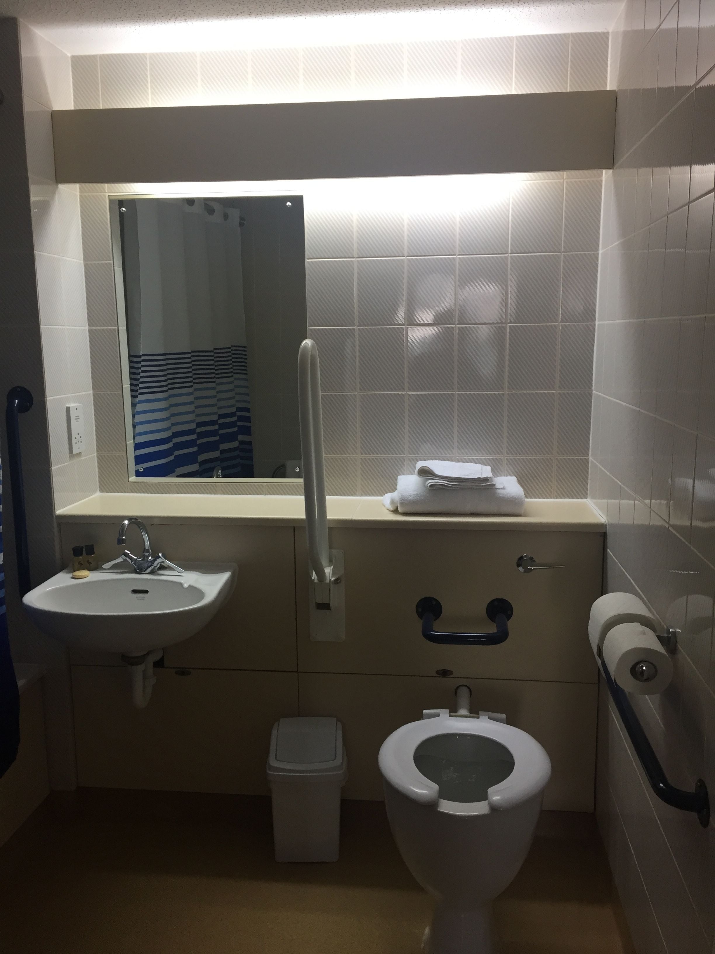 Een compacte badkamer met een wastafel, spiegel, toilet en een prullenbak.