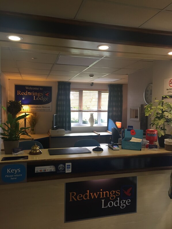 Un mostrador de recepción en Redwings Lodge con un letrero, una computadora, un teléfono y una planta.