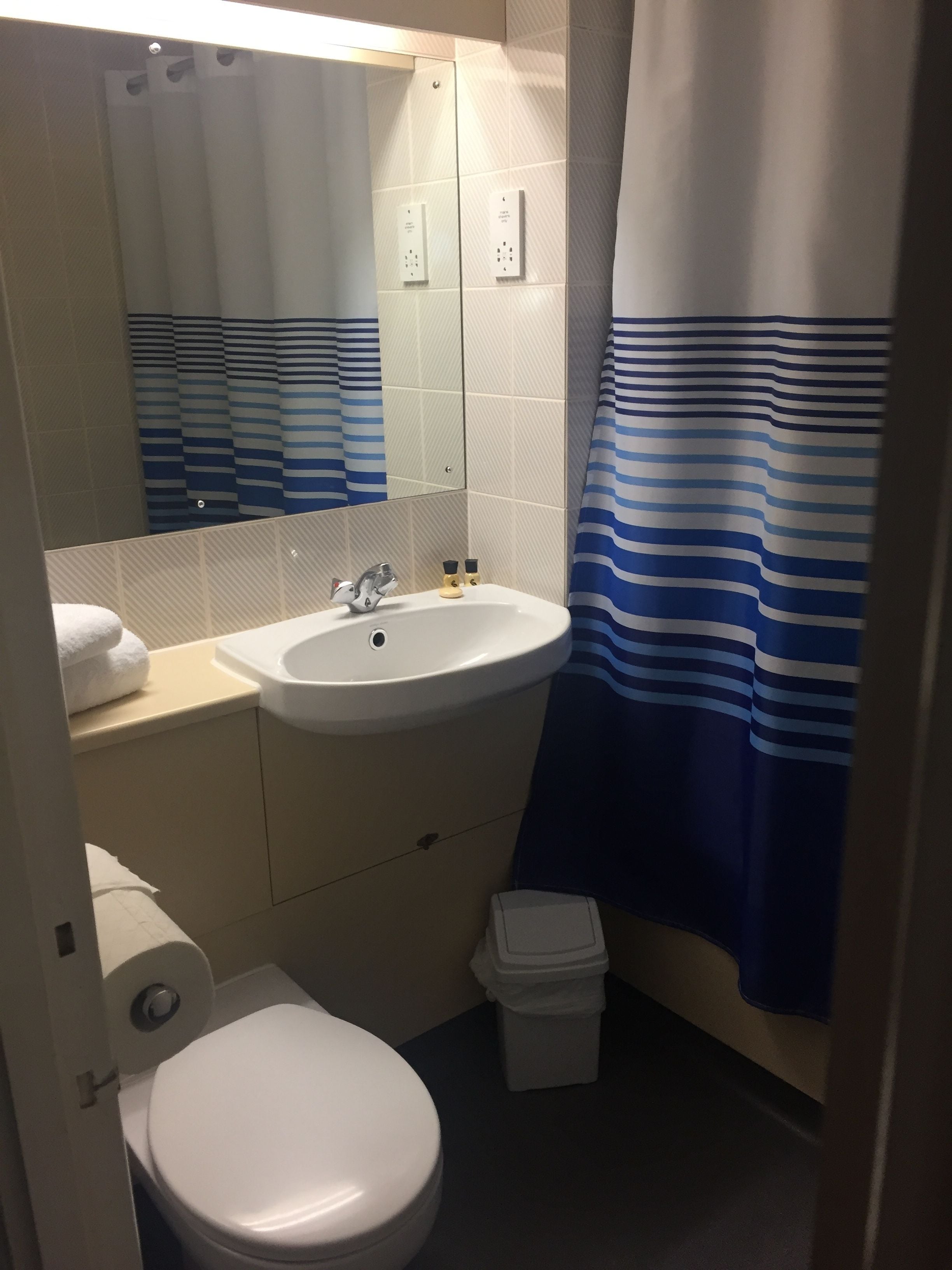 Ein Badezimmer mit einem weißen Waschbecken, einer Toilette, einem Spiegel und einer Duschvorhang mit blauen Streifen.