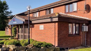A Travelodge hotel with a brick facade, large windows, and a well-maintained lawn. - Travelodge Sleaford (Sleaford)