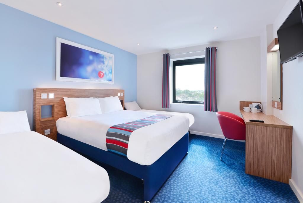 A hotel room with a large bed, a desk, a chair, a TV, and a window with curtains.