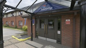 A Travelodge hotel entrance with a brick facade, a glass canopy, and a no smoking sign. - Travelodge Exeter M5 (Exeter)