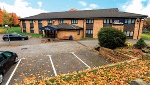 A Travelodge hotel with a brick facade, a covered outdoor seating area, and a parking lot with autumn leaves. - Travelodge Barnsley (Barnsley)