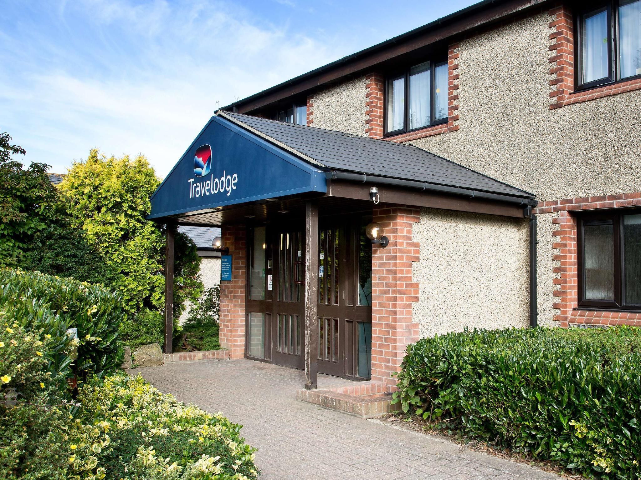 A Travelodge hotel entrance with a blue awning, brick facade, and a pathway leading to the doors.