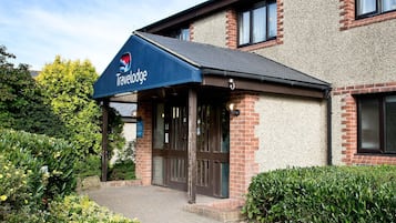 L’entrée d’un hôtel Travelodge, avec un auvent bleu, une façade en briques et un chemin menant aux portes.