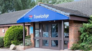 L’entrée d’un hôtel Travelodge, avec un auvent bleu, une façade en briques et une porte en verre transparent.