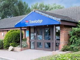 Entrada de un hotel Travelodge con toldo azul, fachada de ladrillo y puerta de cristal transparente.
