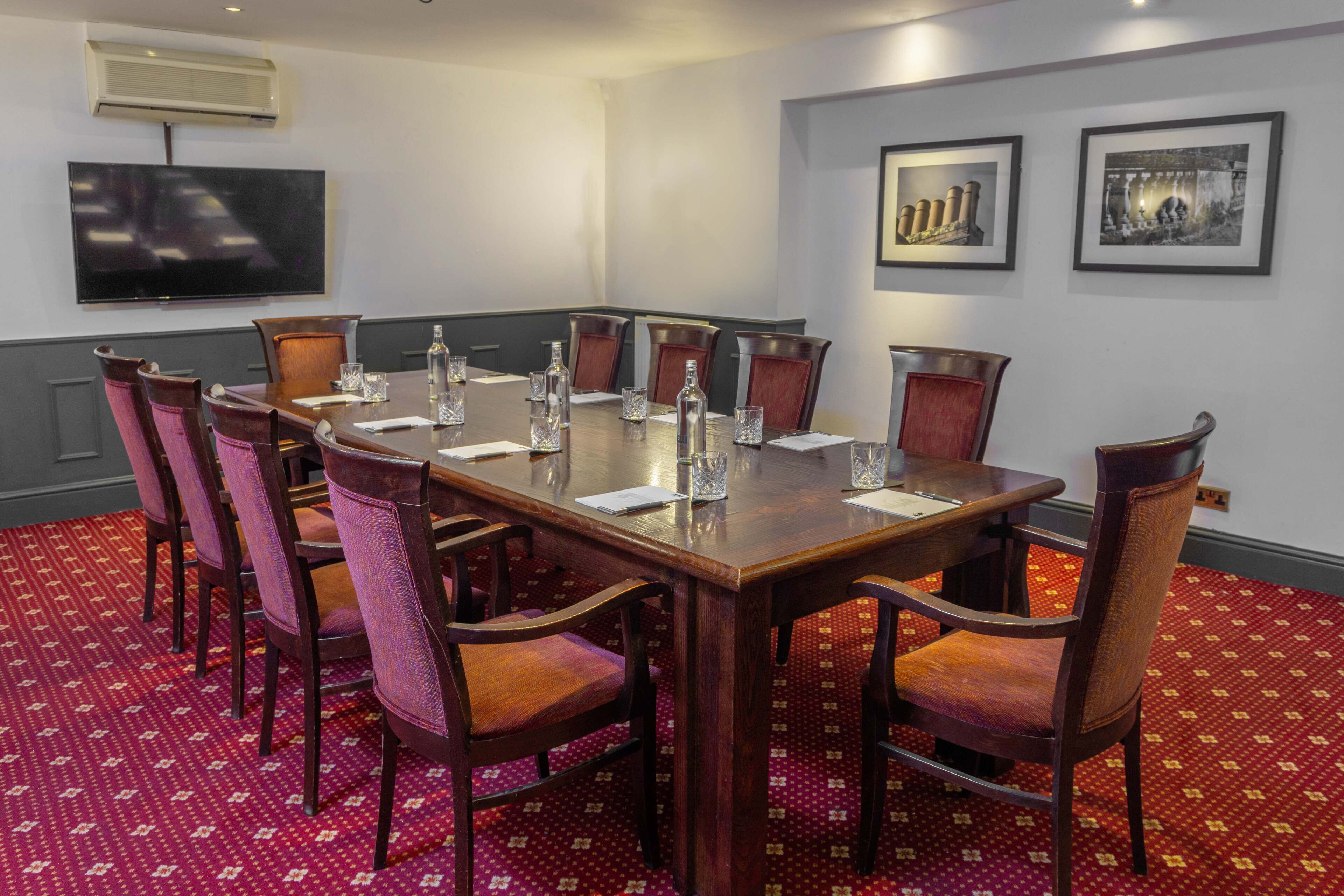 A conference room with a large table, chairs, a flat-screen TV, and framed pictures on the wall.