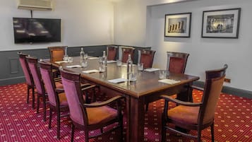 A conference room with a large table, chairs, a flat-screen TV, and framed pictures on the wall.