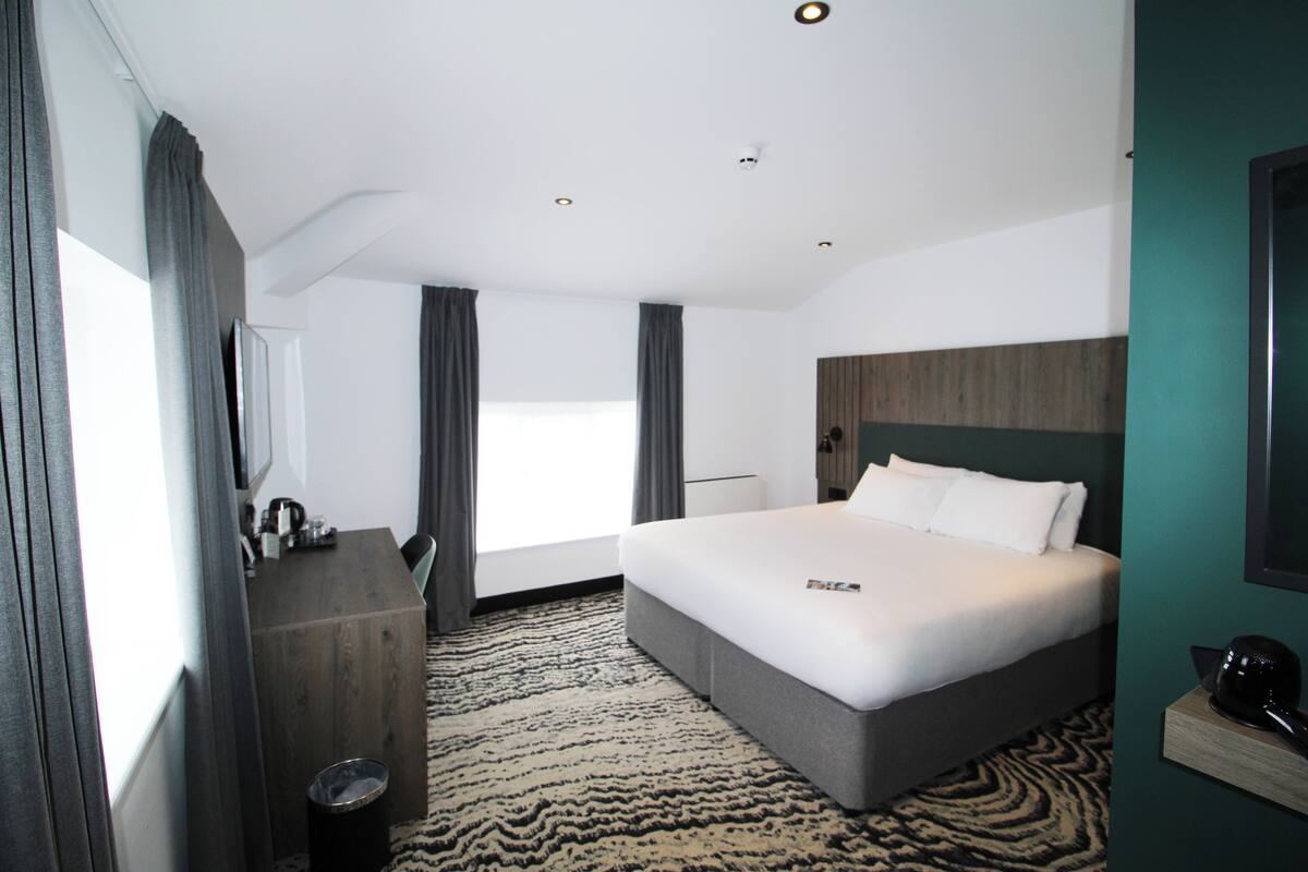 A modern hotel room with a large bed, a wooden dresser, a desk, and a view of the city.