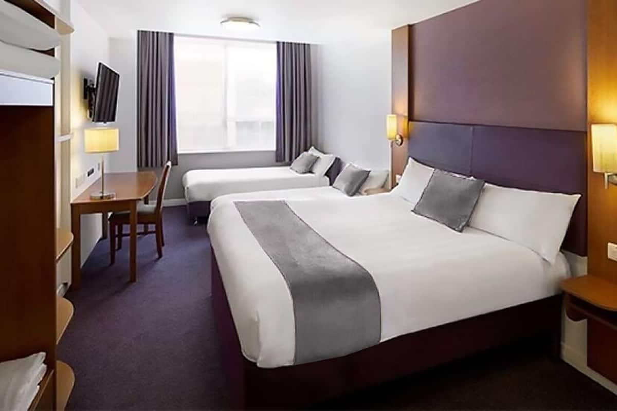 A hotel room with two beds, a desk, a chair, a TV, and a window with curtains.