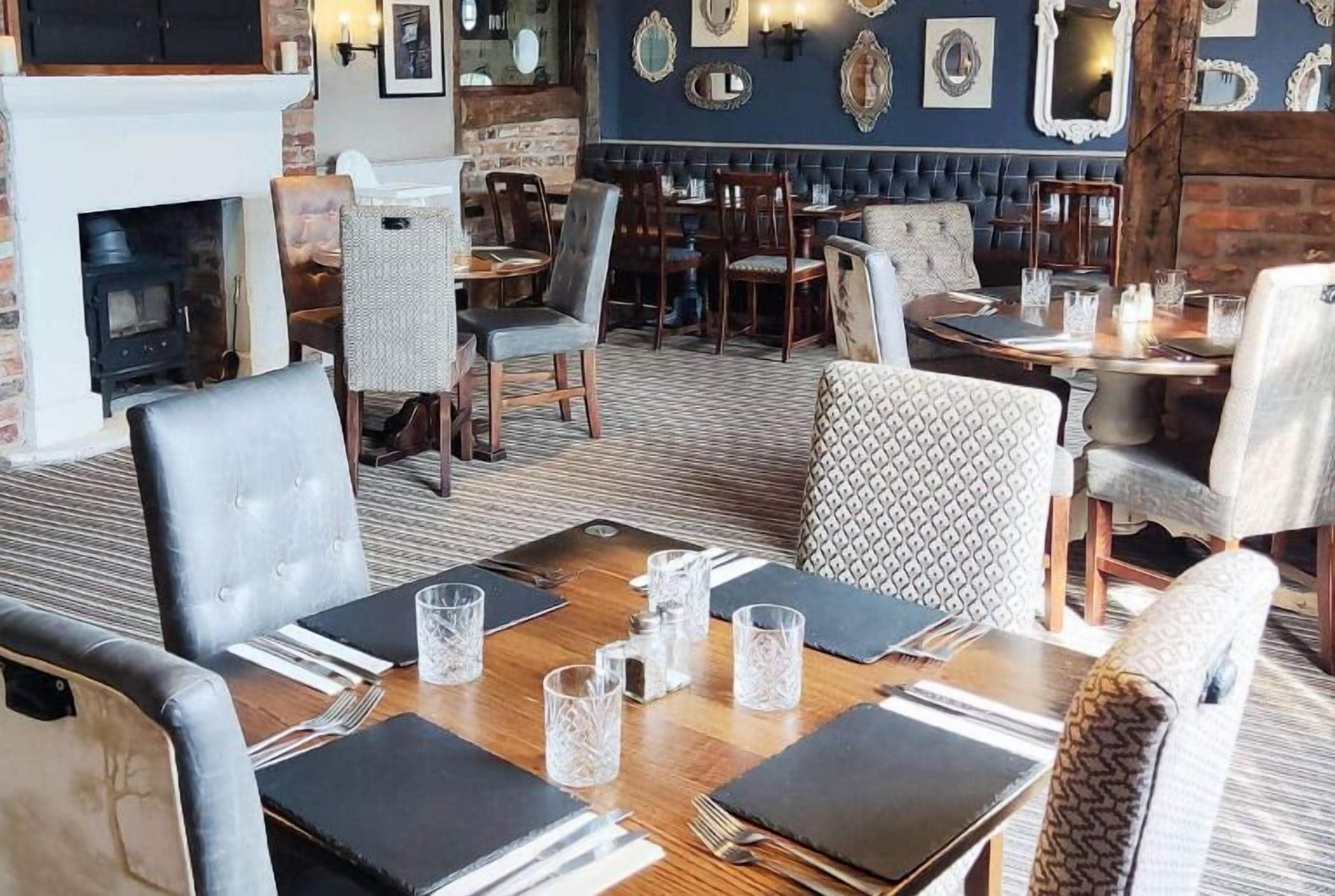 Un restaurant chaleureux avec des tables et des chaises en bois, une cheminée et des miroirs décoratifs sur les murs.