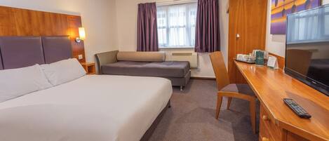 A hotel room with a large bed, a sofa, a desk with a TV, and a window with curtains.