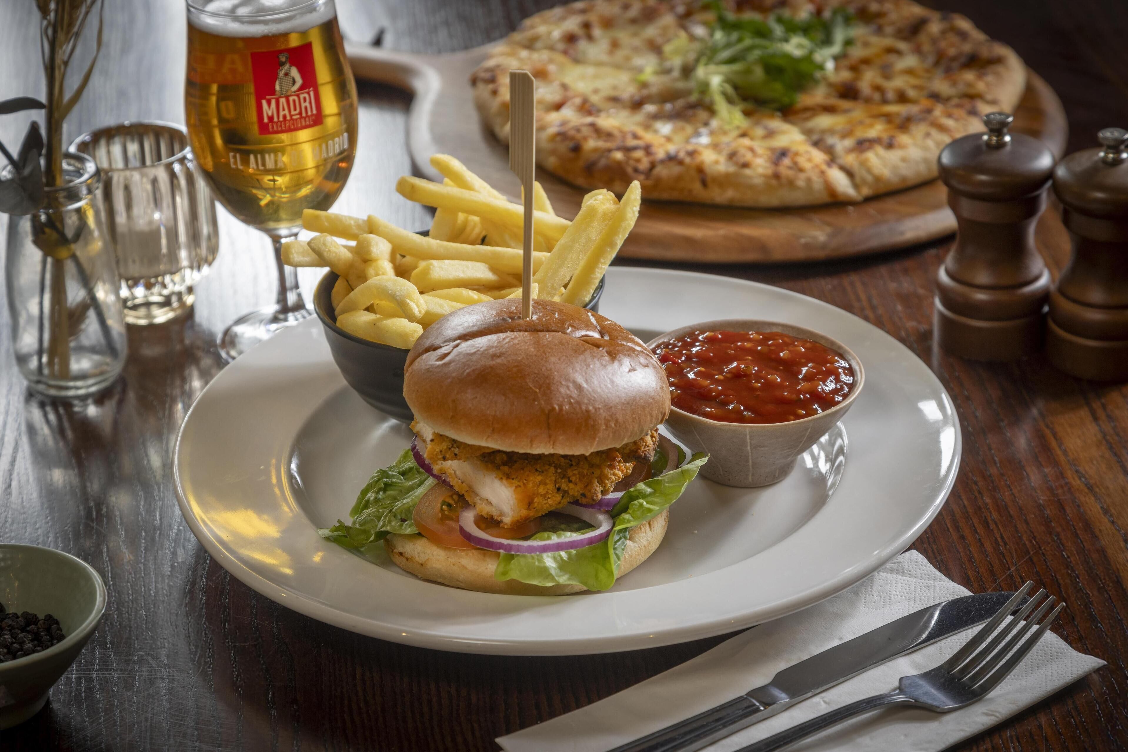 Una comida que incluye una hamburguesa, papas fritas y una pizza sobre una mesa de madera.