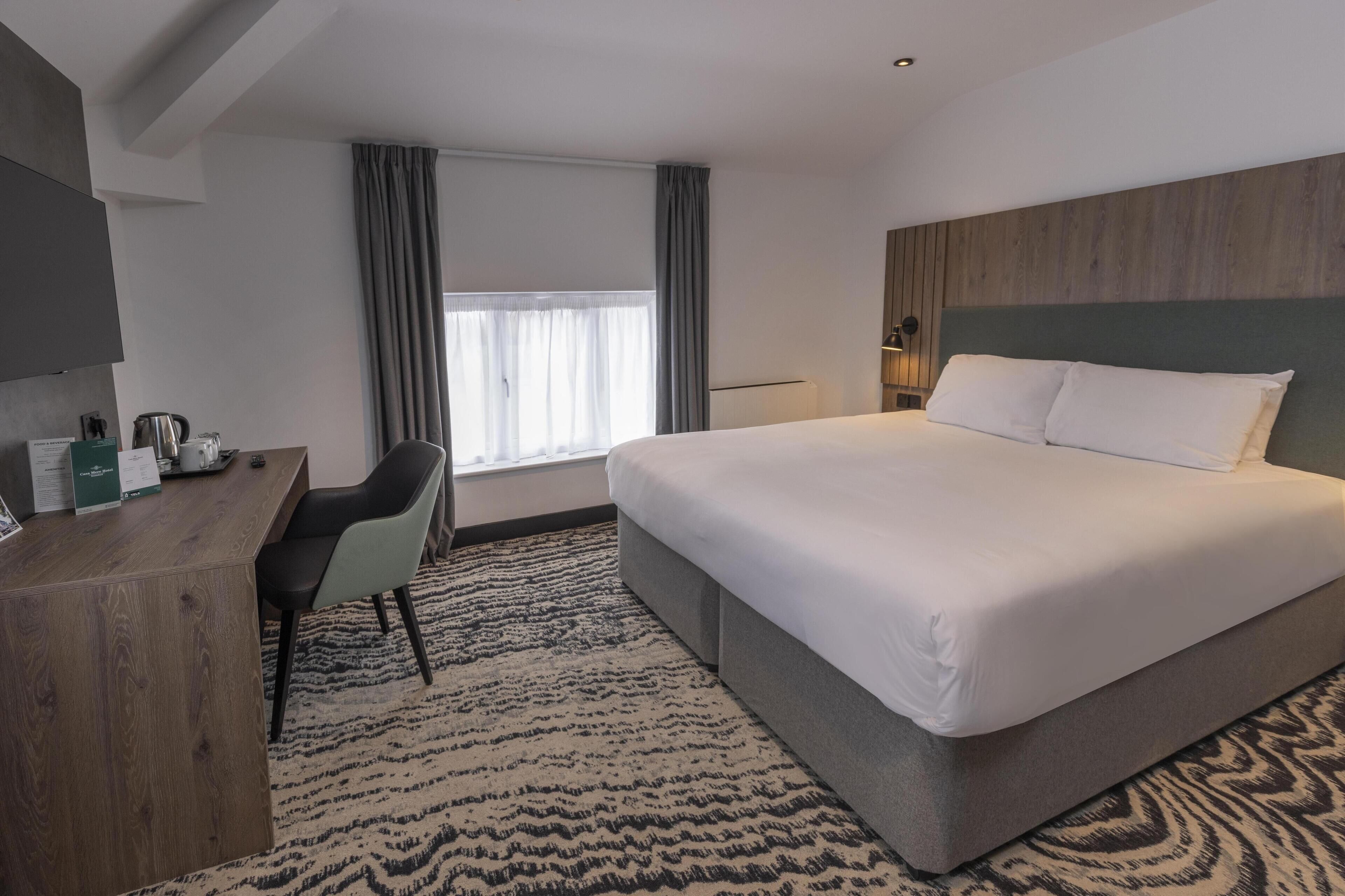 Una habitación de hotel con una cama grande, un escritorio, una silla, un televisor y una ventana con cortinas.