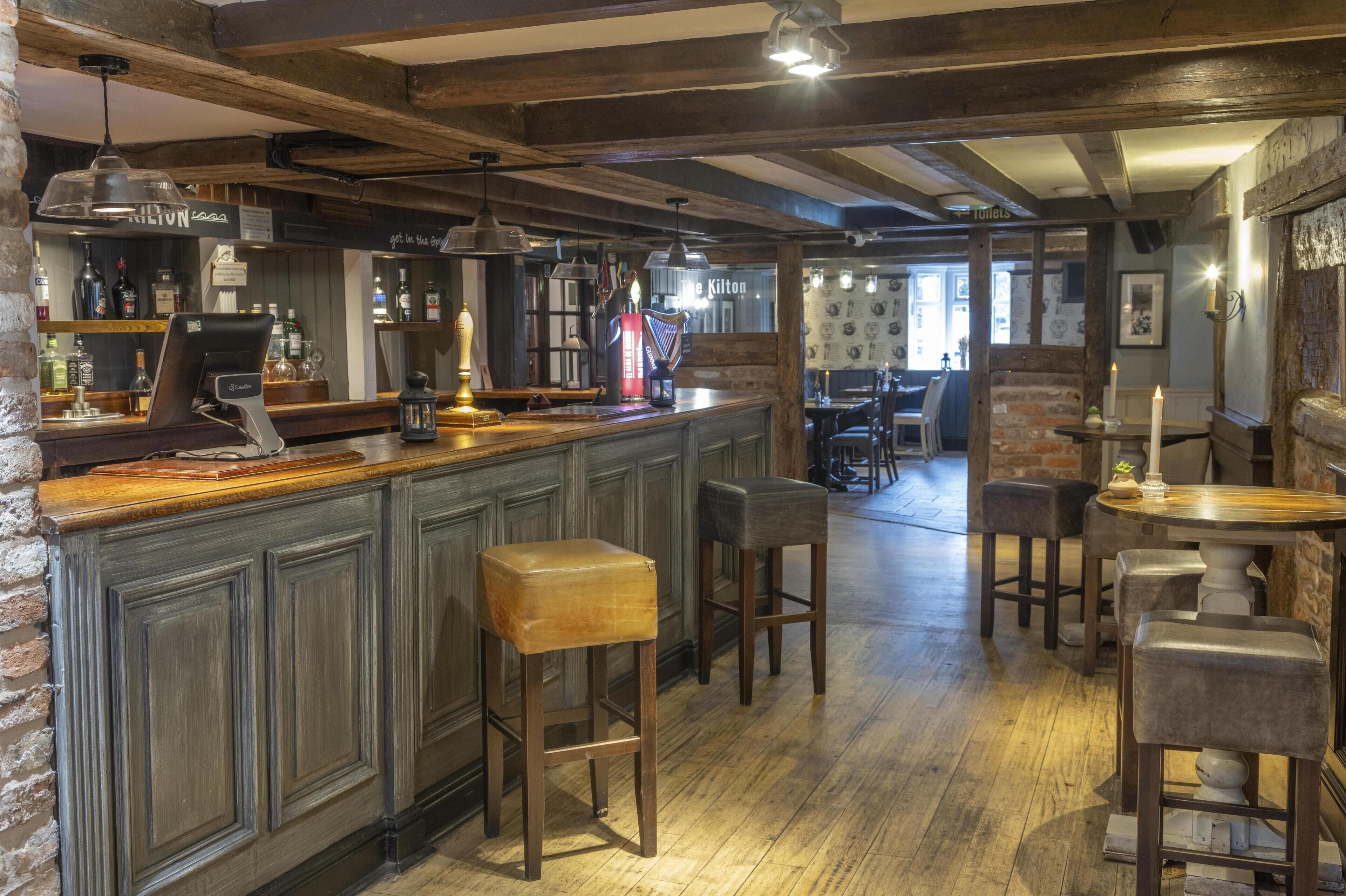Zona de bar con taburetes de madera, una barra con caja registradora y lámparas colgantes.