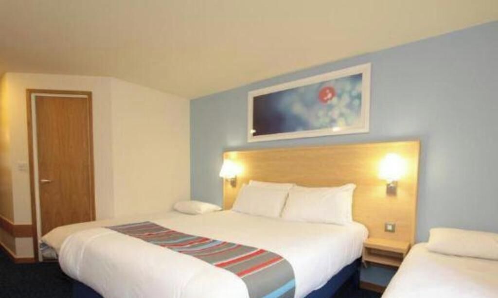 A hotel room with a bed, bedside tables, a headboard, a door, and a wall-mounted artwork.