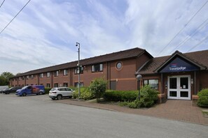 Un hôtel Travelodge avec une façade en briques, une entrée à double porte et un parking rempli de voitures.