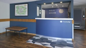 A reception desk with a 'hello & welcome' sign, a framed map on the wall, and a bench in the corner. - Travelodge Stafford M6 (Stone)