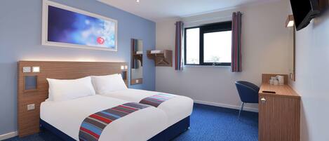 Hotelkamer met een groot bed, een bureau, een stoel, een aan de muur bevestigde televisie en een raam met gordijnen.