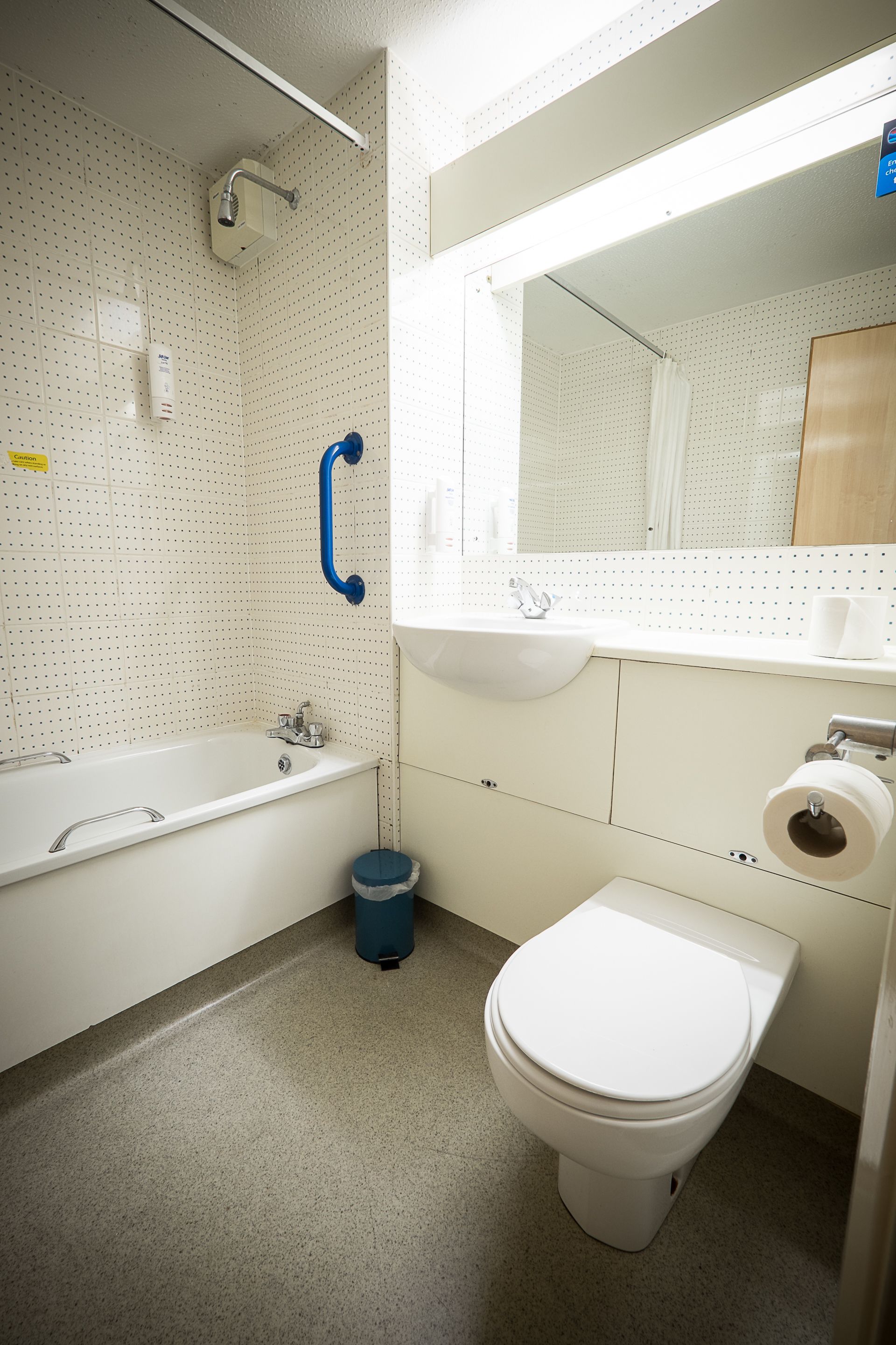 A bathroom with a white bathtub, a white toilet, a blue trash bin, and a mirror above the sink.