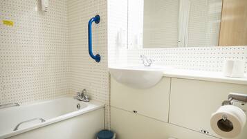 A bathroom with a white bathtub, a white toilet, a blue trash bin, and a mirror above the sink.