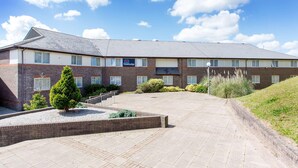 A Travelodge hotel with a brick facade, multiple windows, and a paved courtyard. - Travelodge Saltash (Saltash)