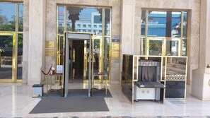 Una entrada de hotel con puerta de vidrio, mostrador de recepción y punto de control de seguridad.
