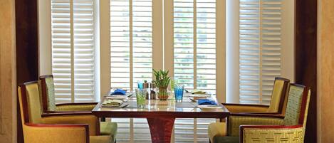 A dining table with four chairs, a vase with flowers, and a window with blinds.