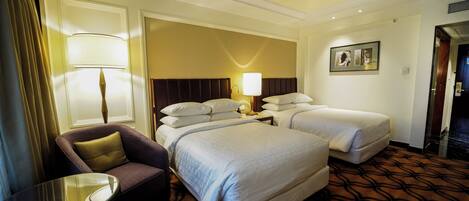 A hotel room with two beds, a chair, a table, and a lamp.
