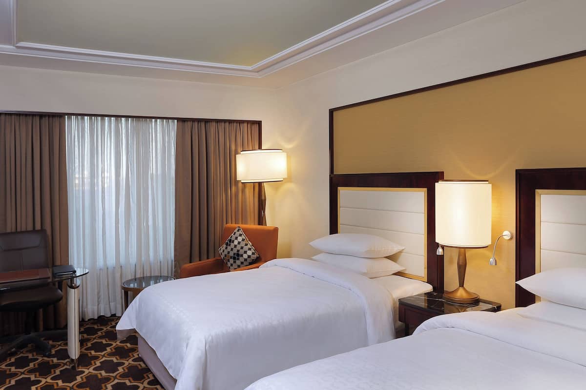 Habitació d'hotel amb dos llits, una taula de treball, una cadira i una làmpada.