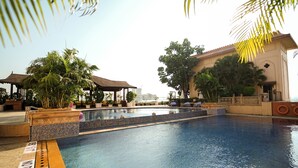 A swimming pool with a tiled edge, surrounded by palm trees and lounge chairs. - Sheraton Grand Pune Bund Garden Hotel (Pune)