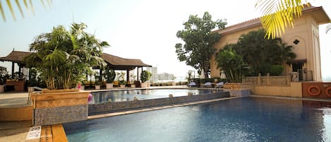 A swimming pool with a tiled edge, surrounded by palm trees and lounge chairs.