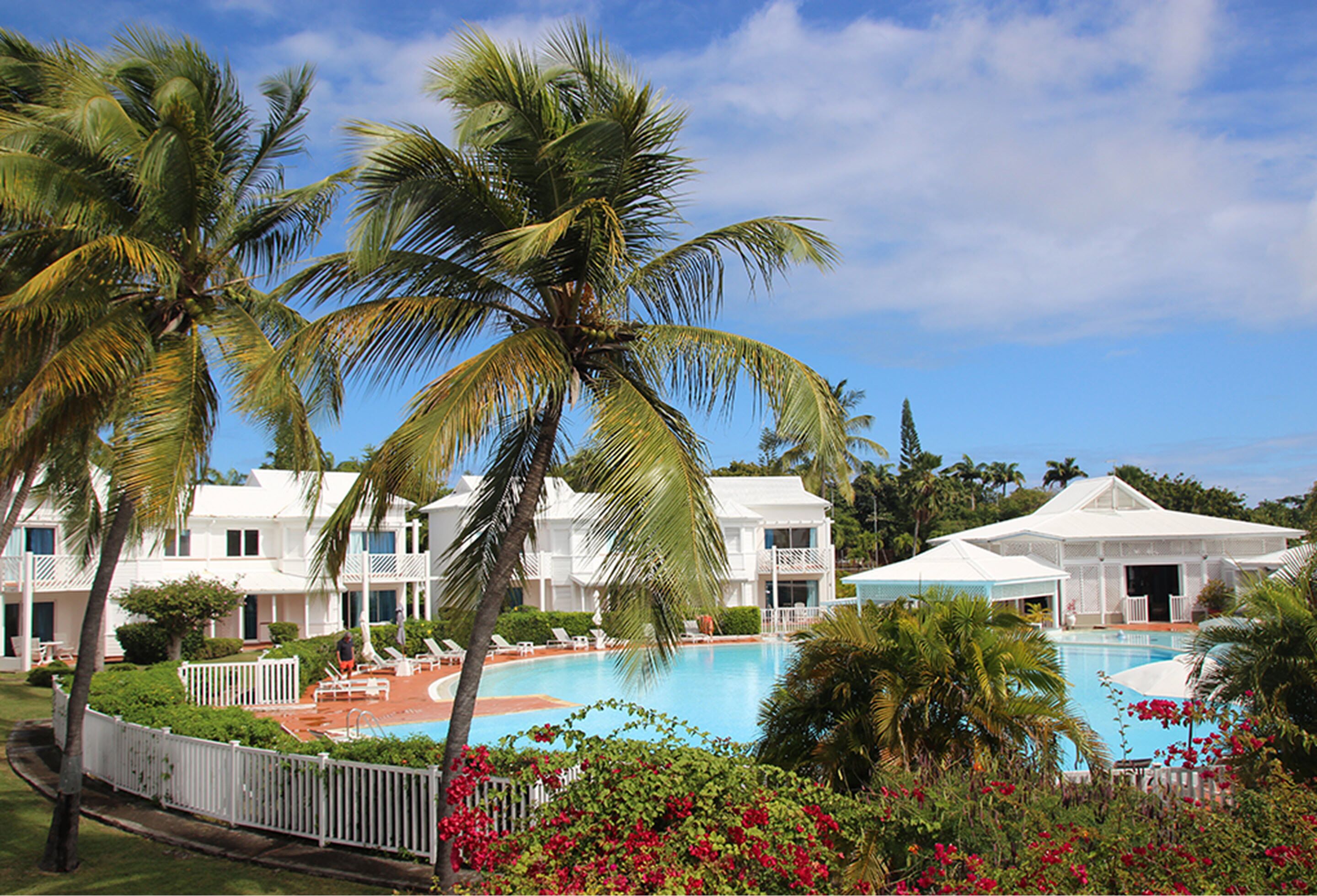 A resort with a swimming pool, palm trees, and white buildings.