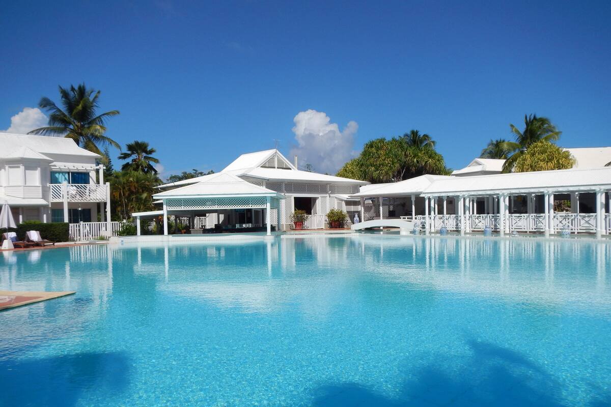 A clear blue pool with white buildings and palm trees in the background.