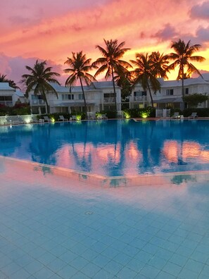 A swimming pool with palm trees and a building in the background. - La Cocoteraie (Saint-François)