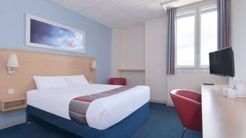 A hotel room with a bed, a desk with a chair, a TV, and a window with curtains.