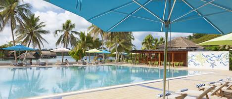 A poolside area with lounge chairs and umbrellas, palm trees, and a thatched-roof structure.
