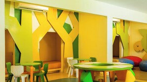 A colorful children's play area with a green and yellow playhouse, multiple seating areas, and a round table with papers. - Holiday Inn Resort Vanuatu by IHG (Port Vila)
